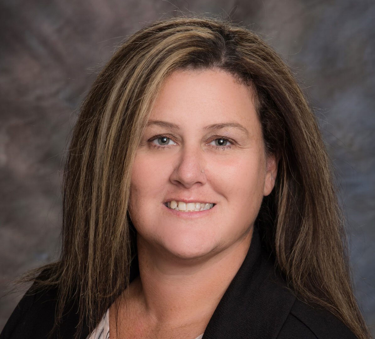 Professional woman with long brown hair smiling against a neutral background.